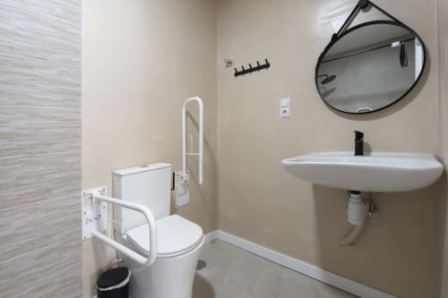 Baño accesible en Studios Sanchis Alicante con barras de apoyo, lavabo, espejo e inodoro