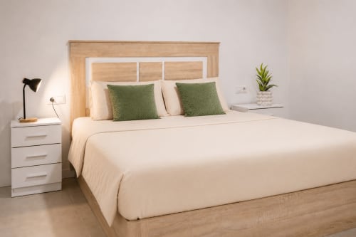 Dormitorio Deluxe Doble en Studios Sanchis, Alicante, con cabecero de madera, ropa de cama crema y almohadas verdes