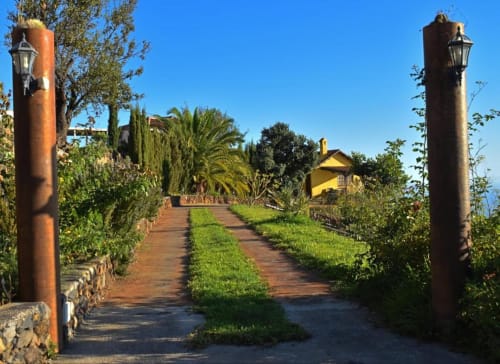 Camino de ladrillo rústico flanqueado por altos pilares que conducen a Villa Las Flores en Tijarafe, La Palma, con edificio amarillo