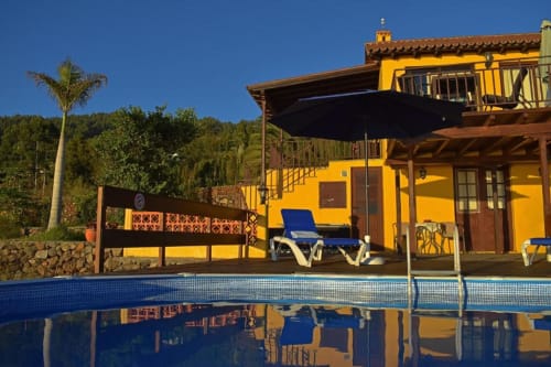 Villa amarilla luminosa con piscina, tumbonas azules y vistas a las montañas en Tijarafe, La Palma