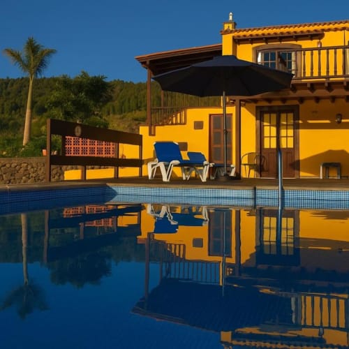 Villa Las Flores en Tijarafe con arquitectura amarillo brillante, piscina, tumbonas azules y vistas a las montañas