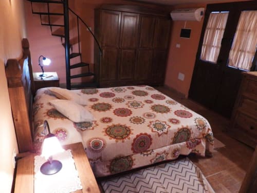 Amplio dormitorio de villa en Rural La Palma con ropa de cama estampada, muebles de madera, paredes coral y escalera de caracol