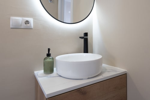Espejo iluminado con lavamanos blanco redondo y grifo negro en el moderno lavabo de Studios Sanchis Alicante