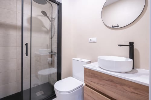Baño moderno en Studios Sanchis Alicante con ducha de paso, lavabo blanco de cerámica y tocador de madera