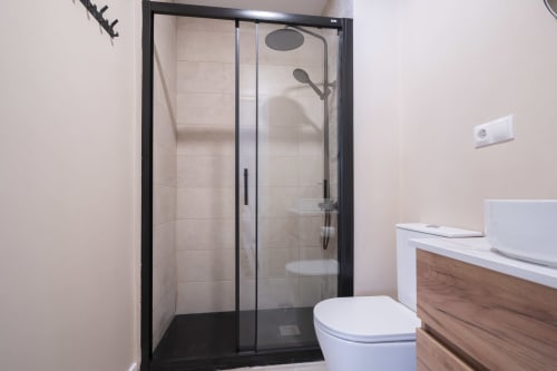 Baño moderno en Estudio Doble Deluxe de Studios Sanchis, Alicante, con ducha de cristal con marco negro y acabados blancos