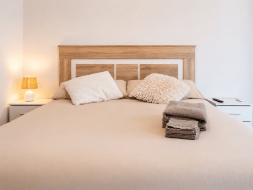 Moderna habitación de hotel en Studios Sanchis, Alicante, con cabecero de madera, ropa de cama neutral, cojines decorativos y toallas dobladas