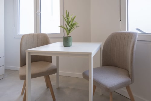 Zona de comedor minimalista en Studios Sanchis Alicante con mesa blanca, sillas beige y plantas decorativas