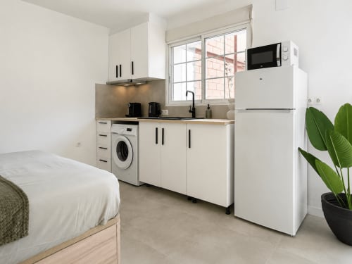 Pequeña cocina con electrodomésticos blancos, lavadora y cama en habitación de hotel en Alicante