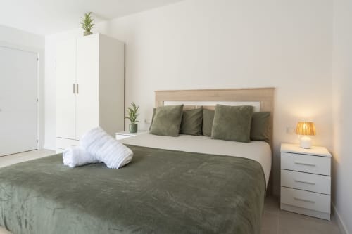 Dormitorio moderno en Studios Sanchis Alicante con ropa de cama aceituna, cabecero de madera, armario blanco y toques verdes