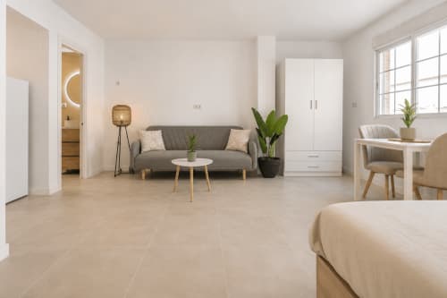 Moderno apartamento tipo estudio en Studios Sanchis, Alicante, con sofá gris, armario blanco y suelo de baldosas beige