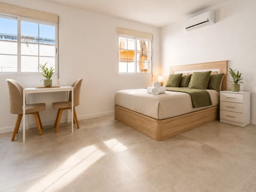 Luminosa habitación estudio en Studios Sanchis, Alicante, con cama de madera, escritorio y mobiliario moderno con vistas a la piscina