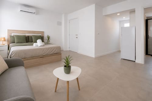 Habitación de estudio moderno en Studios Sanchis de Alicante con cama de madera, zona de estar y planta sobre mesa blanca