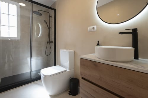Baño moderno en Studios Sanchis, Alicante con lavabo tipo recipiente, grifo negro, ducha de lluvia, inodoro y espejo redondo