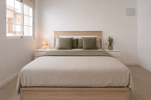 Luminoso estudio en Studios Sanchis Alicante con cama de madera, ropa de cama blanca y almohadas verde oliva