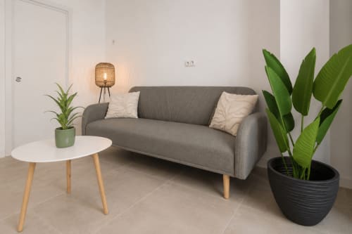 Sala de estar de estudio moderno en Studios Sanchis Alicante con sofá gris, mesa blanca, plantas en maceta y lámpara tejida