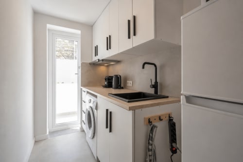Cocina moderna en estudio Studios Sanchis con muebles blancos, fregadero negro, encimera de madera y lavadora en Alicante
