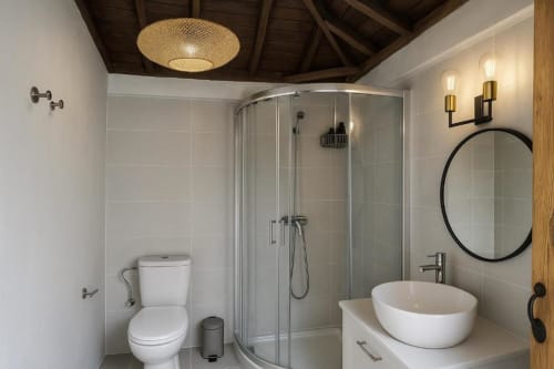 Baño moderno en villa Nexus de Rural La Palma con ducha de lluvia, espejo redondo y lavabo blanco de cerámica