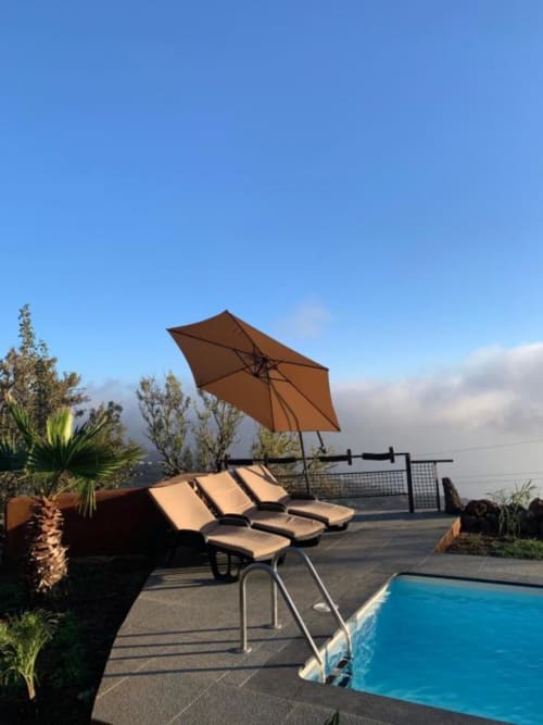 Terraza soleada de Villa El Topo con tumbonas, sombrilla marrón, piscina privada y vistas a las montañas en La Palma
