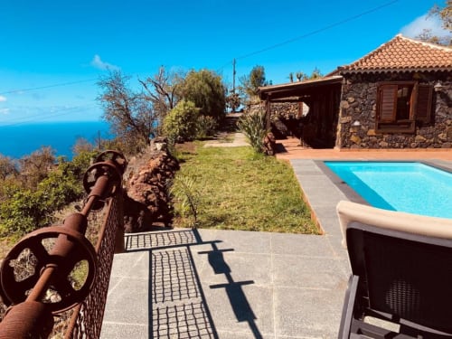 Terraza con piscina de Villa El Topo, vistas al océano, casa de piedra, barandillas oxidadas y horizonte de mar azul en La Palma