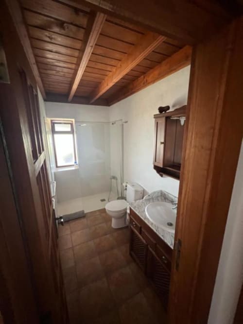 Baño moderno en Villa El Topo, La Palma rural, con vigas de madera, lavamanos, inodoro y ducha de cristal
