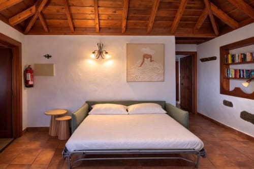Dormitorio moderno en Villa El Topo, La Palma Rural con techo de vigas de madera, sofá cama verde y decoración rústica