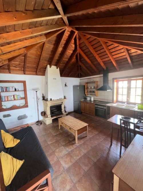 Zona de estar abierta en Villa El Topo con vigas de madera, chimenea, cocina y comedor con vistas al jardín
