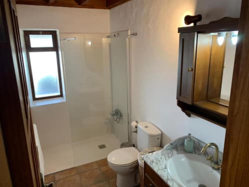 Baño moderno en Villa El Topo con ducha de cristal, inodoro, tocador de mármol, gabinete espejo de madera y ventana
