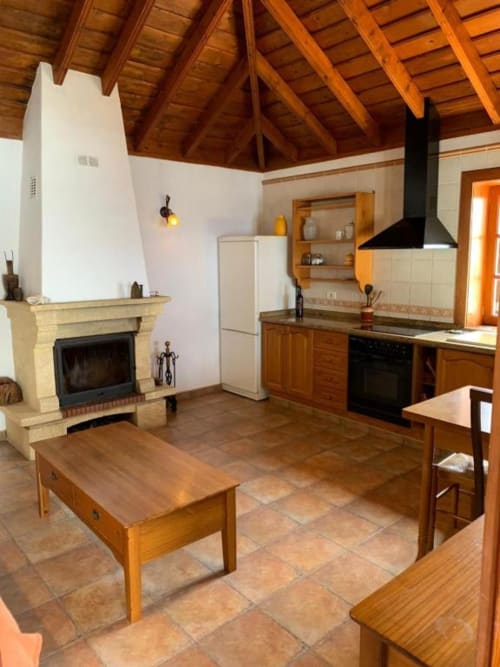 Zona de estar de Villa El Topo con chimenea, cocina, vigas de madera y mobiliario rústico en La Palma, España