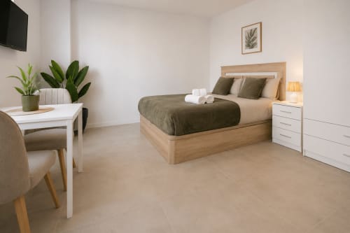 Dormitorio de estudio moderno en Studios Sanchis en Alicante con cama de madera, muebles blancos y plantas verdes
