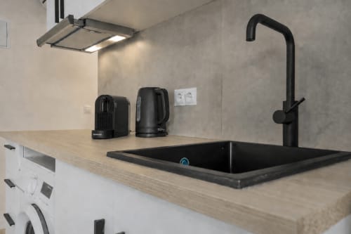 Área de cocina moderna en habitación del hotel Studios Sanchis, Alicante, con fregadero negro, grifo y electrodomésticos sobre mostrador de madera