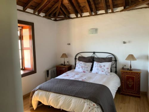 Dormitorio luminoso en Villa Awara, La Palma rural, con cama de hierro, ropa de cama floral, mesitas de madera y vigas vistas