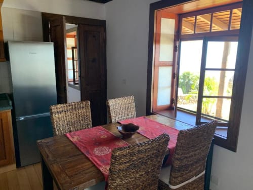 Comedor de Villa Awara con sillas de mimbre, mesa de madera, salvamanteles rojos, refrigerador de acero inoxidable y acceso a terraza