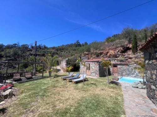 Patio de Villa Awara con tumbonas, edificios de piedra, zona de piscina y vistas a la montaña en El Pinillo, La Palma