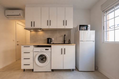 Cocina compacta y moderna en estudio Studios Sanchis Alicante con muebles blancos, lavadora y refrigerador