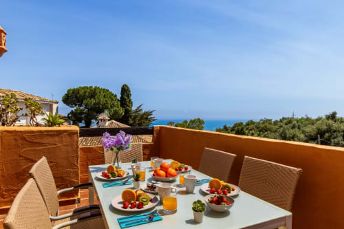 Beachfront villa terrace in Benalmádena with breakfast spread, purple flowers, and Mediterranean Sea view