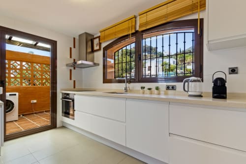 Modern kitchen with white cabinets, wooden beams, and views of Benalmádena landscape in Ayma Villa Cielo y Mar