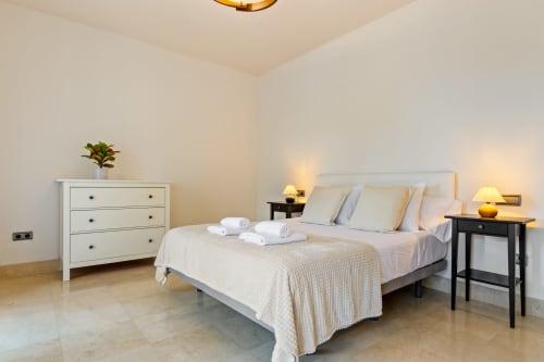 Bright master bedroom in Benalmádena villa with queen bed, white linens, bedside lamps, cream dresser, and tiled flooring