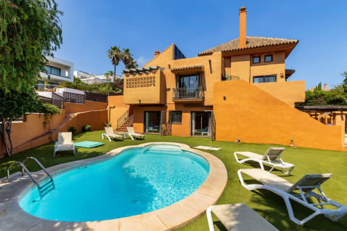 Luxury orange villa in Benalmádena with kidney-shaped pool, lounge chairs, and manicured gardens