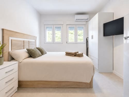Moderno dormitorio de estudio en Studios Sanchis, Alicante, con cama de madera, smart TV y ventanales con vistas a la ciudad