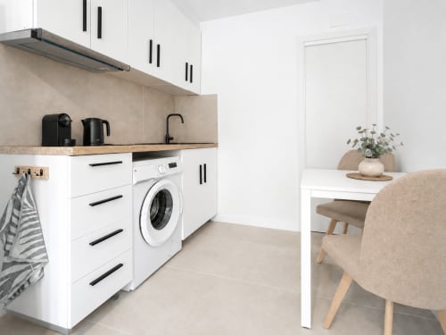 Cocina moderna de estudio con armarios blancos, lavadora y zona de comedor en el hotel Studios Sanchis de Alicante