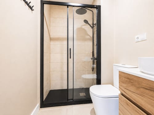 Baño moderno en Studios Sanchis en Alicante con cabina de ducha de cristal con marco negro y alcachofa de lluvia