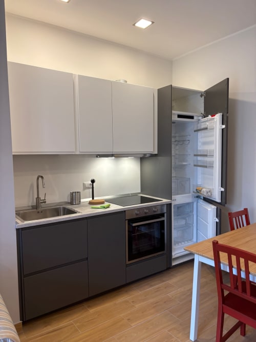 Cucina moderna nell'appartamento milanese con pensili bianchi, basi nere, elettrodomestici in acciaio inox e tavolo in legno