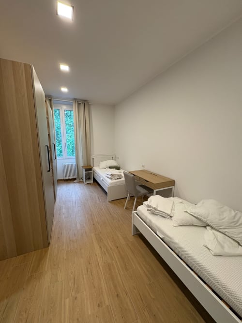 Camera da letto moderna in appartamento milanese con due letti, armadio in legno, scrivania e porte-finestre sul balcone