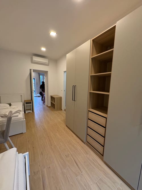 Camera da letto moderna in appartamento milanese con pavimento in legno, guardaroba integrato, scaffali e arredi bianchi
