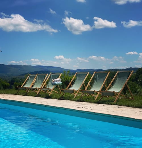 Rangée de transats en bois près de la piscine turquoise du Château de Vaux Morvan, avec la campagne bourguignonne et ses collines ondulantes sous un ciel bleu