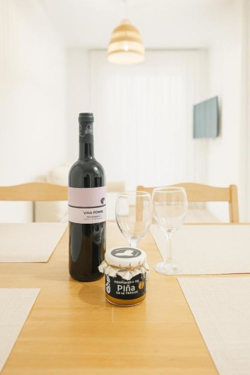 Botella de vino y frasco local sobre mesa de comedor de madera en apartamento El Hierro con copas de vino y lámpara colgante