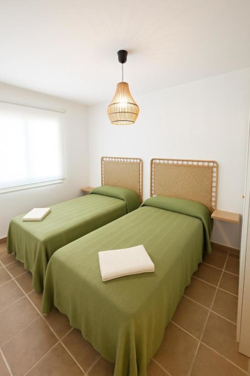 Dos camas individuales con ropa de cama verde y cabeceros tejidos en luminoso dormitorio de Rural La Palma, La Restinga