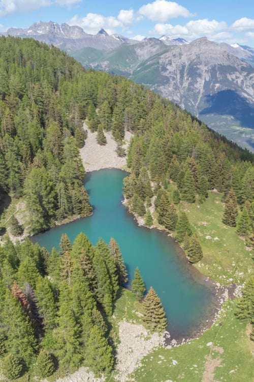 Lac alpin turquoise entouré de forêt de conifères dense et montagnes enneigées près de Méolans-Revel