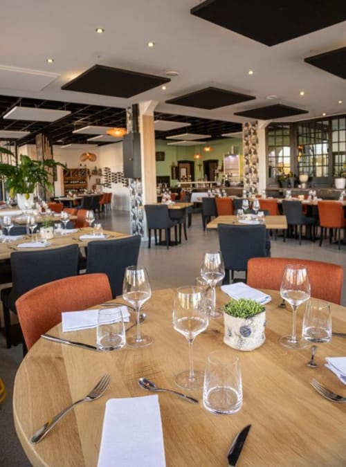 Modern restaurant dining room at Hôtel Restaurant Le S'Y with round wood tables, orange and black chairs, and contemporary