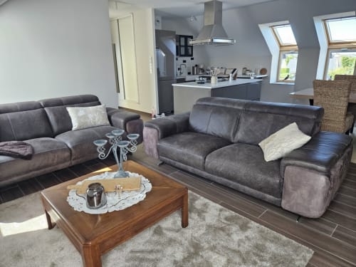Salon moderne avec canapés en cuir gris, table en bois et cuisine ouverte de l'appartement Cap à l'Ouest au Clos De La Côte